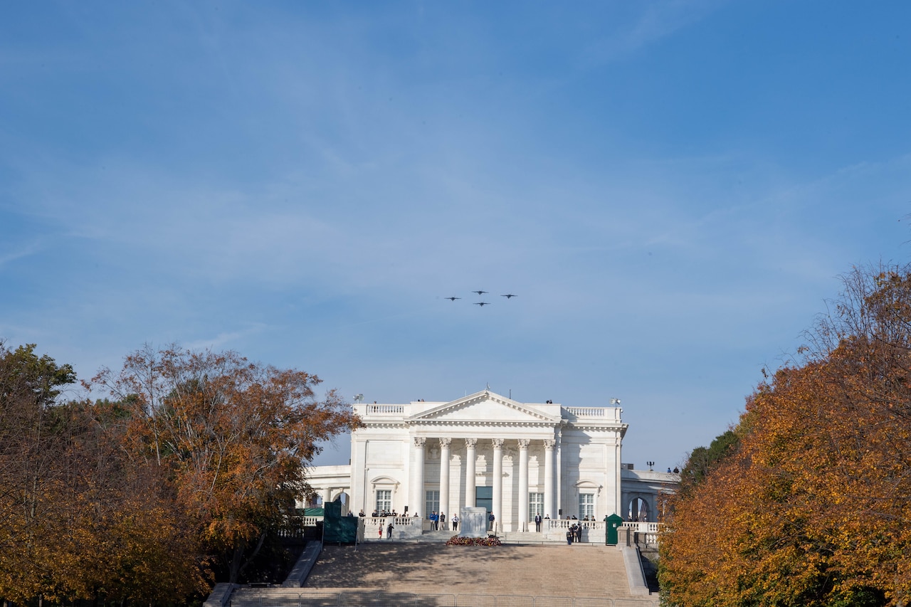 Four jets fly above a large building.