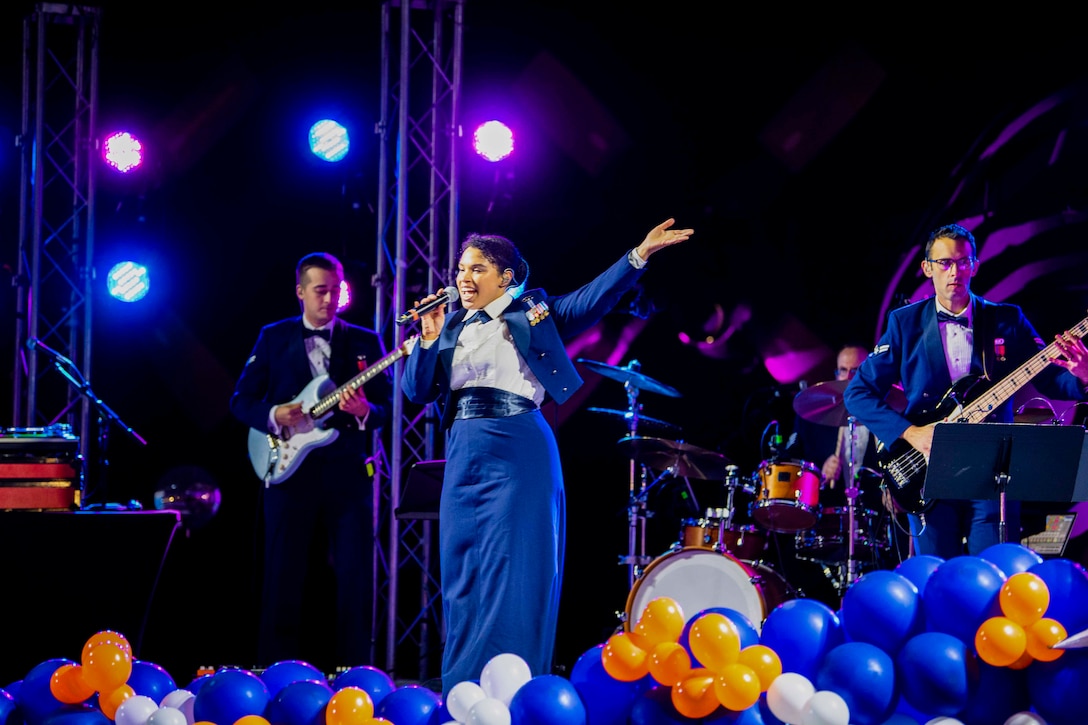 An airman sings into a microphone while three others play instruments behind.