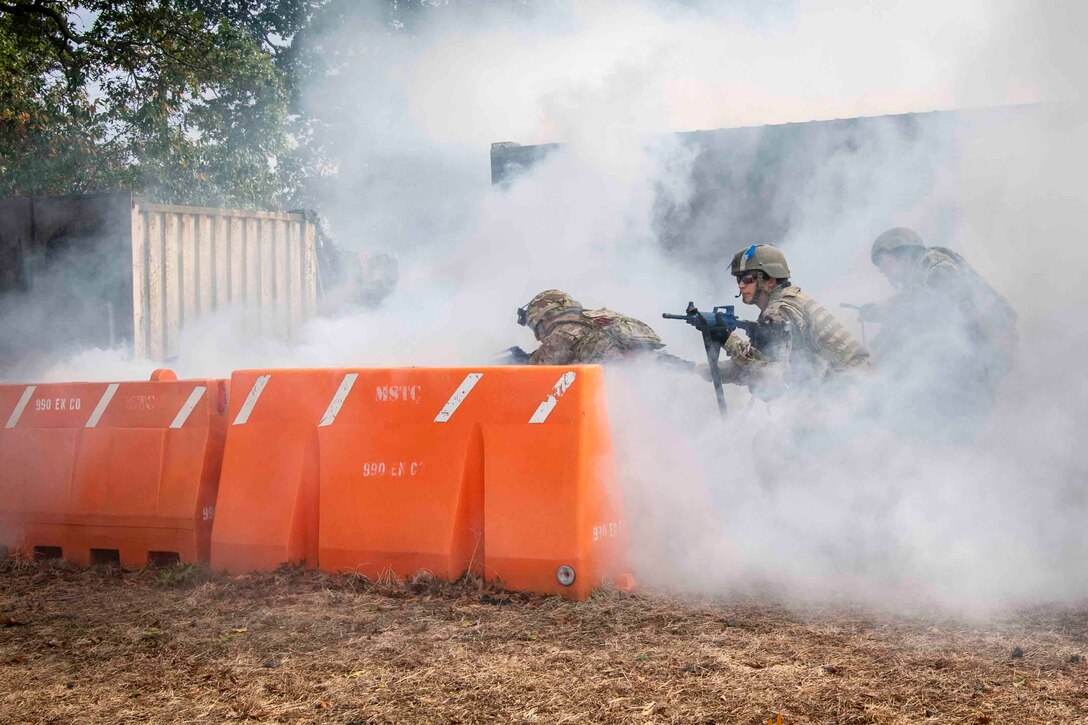 Airmen move through smoke in front of an orange barrier.