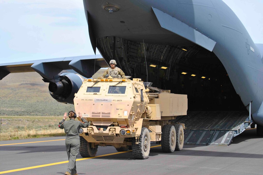 A soldier signals toward another soldier in a military vehicle.