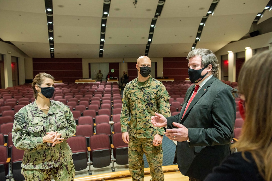 Commander Fabry in a Navy utility uniform with Maj. Kyle Huston in a Marine Corps utility uniform speaking to a older gentleman in a suit.