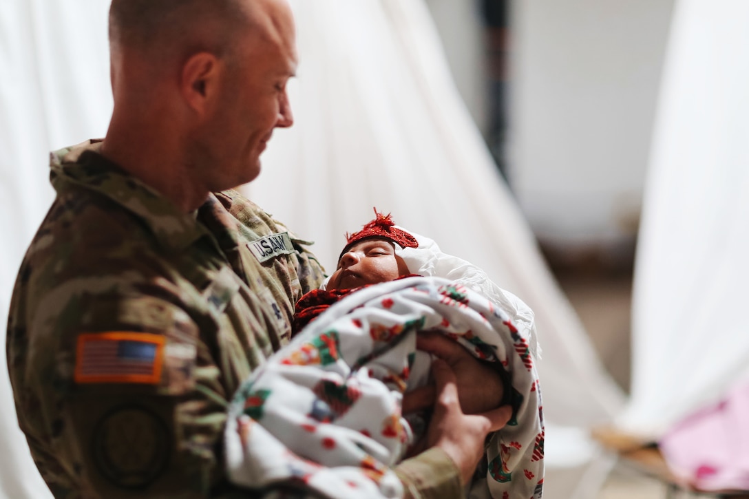 A soldier looks down and smiles while holding an Afghan baby.