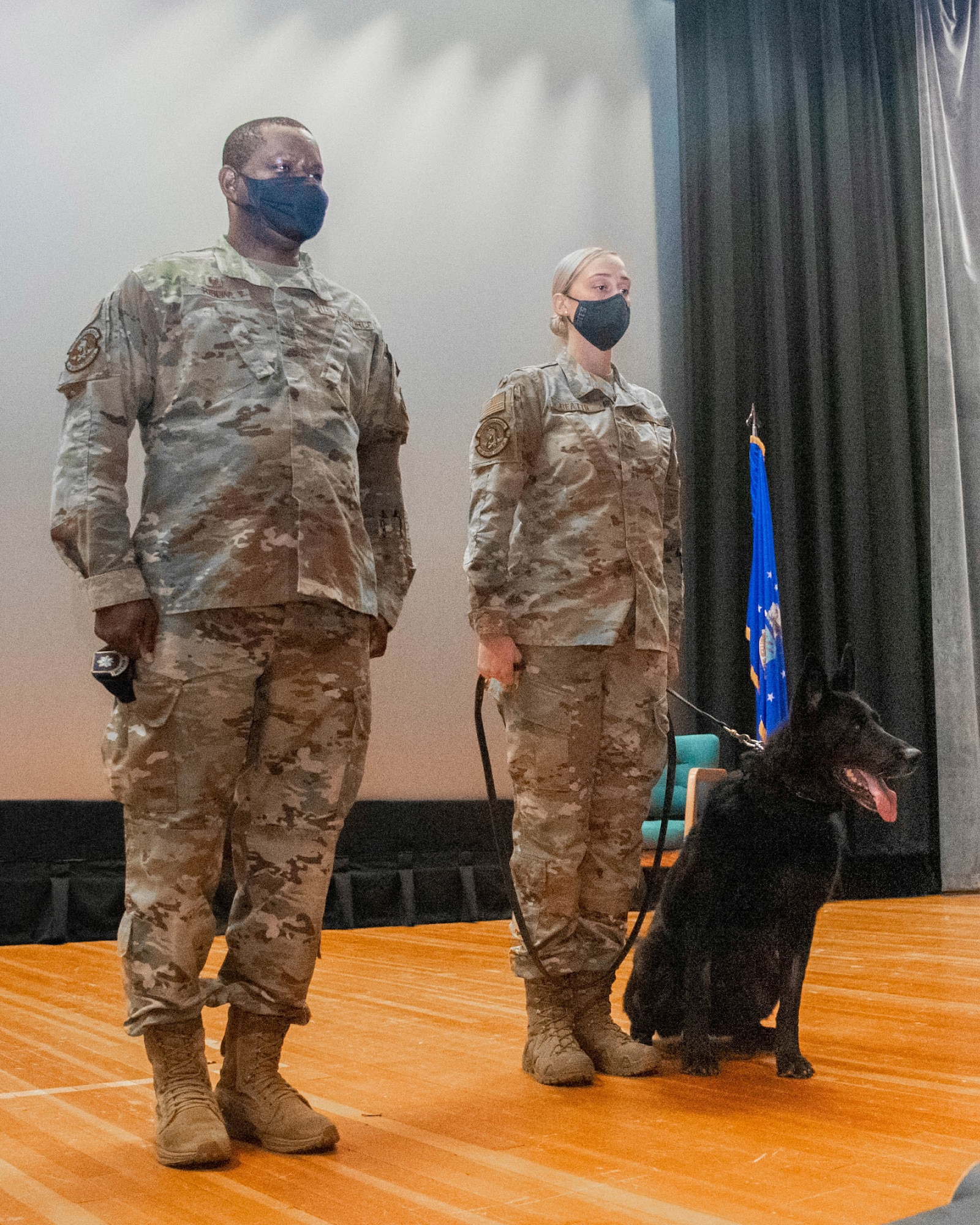 Lt. Col. Schneider Rislin, left, 436th Security Forces Squadron commander, stands with Tech. Sgt. Ashley Beattie, 436th SFS unit deployment manager, and Military Working Dog Vito W285 as the MWD certificate of meritorious service is read during Vito’s retirement ceremony at the base theater on Dover Air Force Base, Delaware, Nov. 9, 2021. During his six years of service, MWD Vito helped provide drug detection sweeps for 9,000 vehicles, 300 facilities and assisted the Air Force Office of Special Investigations in a dorm raid and successfully found drugs and drug paraphernalia. (U.S. Air Force photo by Tech. Sgt. Nicole Leidholm)