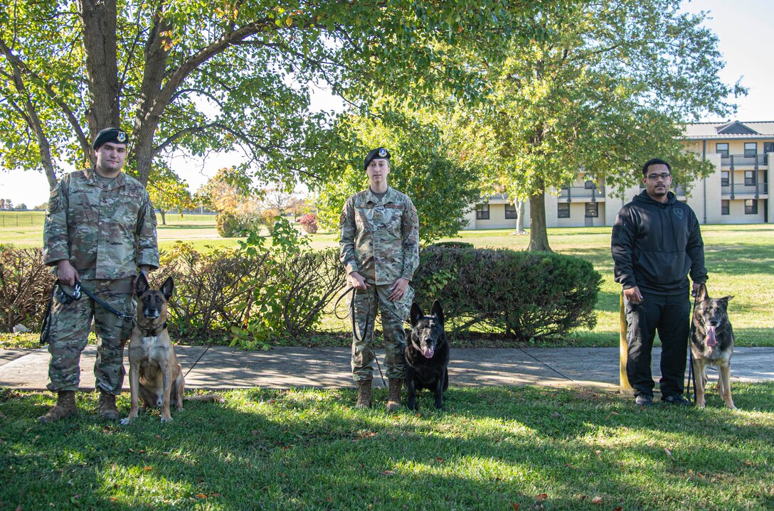 From the left, Staff Sgt. Dylan Bulick, 436th Security Forces Squadron Military Working Dog handler with MWD Johny, Tech. Sgt. Ashley Beattie, 436th SFS unit deployment manager with MWD Vito, and Malcolm Young, a former 436th SFS MWD handler with MWD Ramos, pose for a photo after their K-9s retirement from working dog service at the base theater on Dover Air Force Base, Delaware, Nov. 9, 2021. The MWDs were retired after more than six years of dedicated service and were no longer medically able to complete their job. (U.S. Air Force photo by Tech. Sgt. Nicole Leidholm)