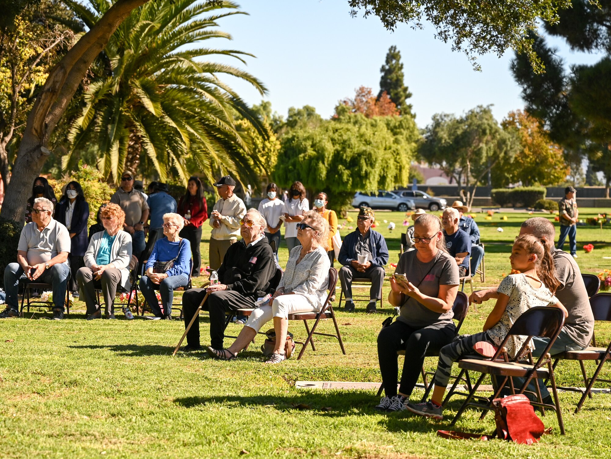 Crowd of people standing and sitting outside on chairs