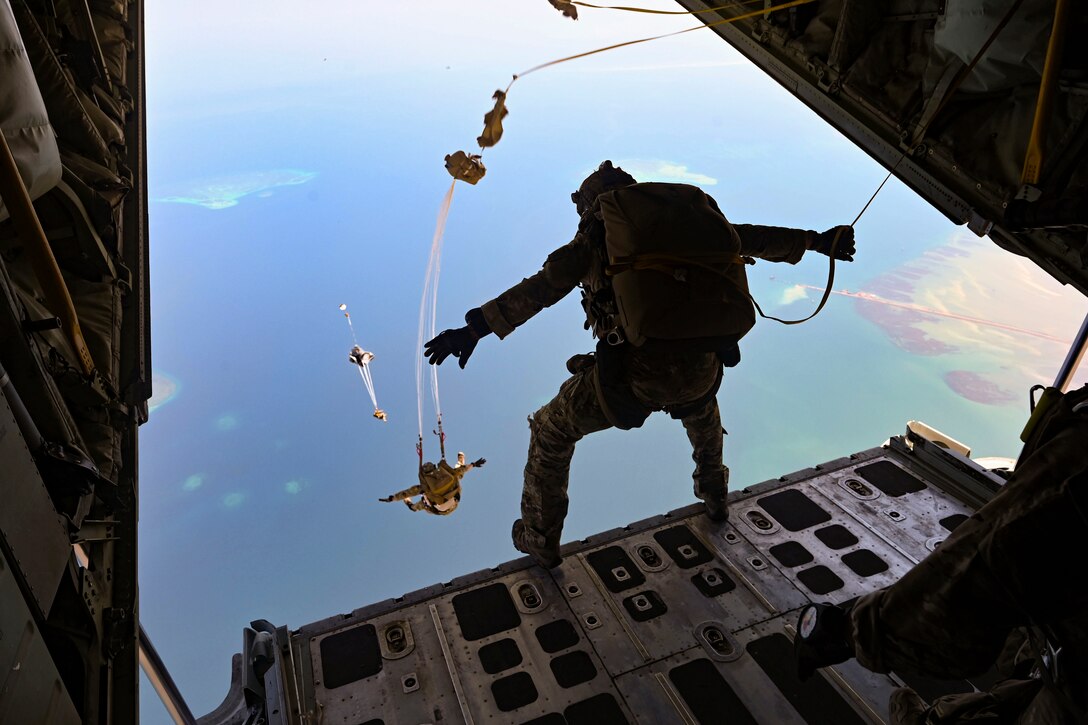 Airmen jump out of an aircraft wearing parachutes.