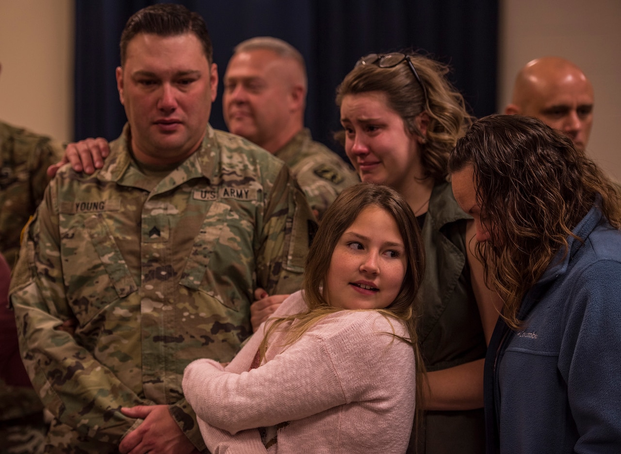A distraught-looking soldier stands beside three teen girls, one of whom is crying.