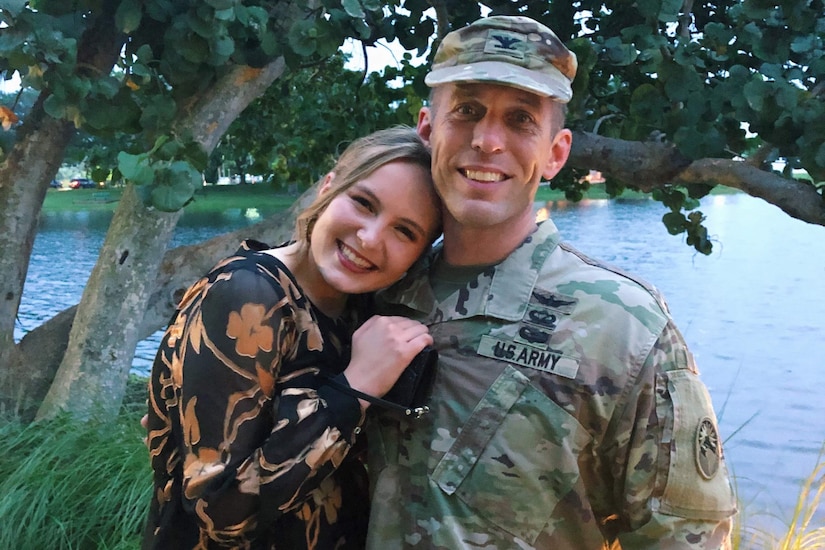 A girl hugs a soldier in front of a lake.