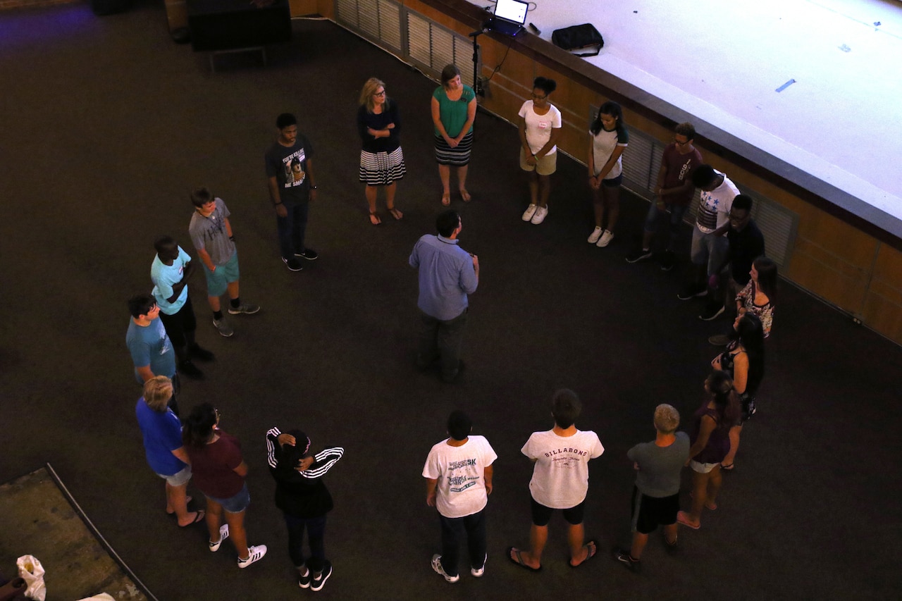 A man stands in the middle of a circle of teenagers.