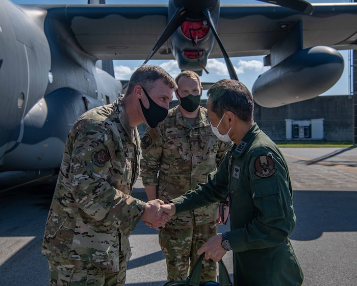 U.S. Air Force Col. Shane Vesely, left, 353rd Special Operations Wing commander, shakes hands with Japan Air Self-Defense Force Col. Hidenori Ichigi, right, 2nd Tactical Airlift Group commander, in front of a U.S. Air Force MC-130J Commando II while U.S. Air Force Maj. Jacob McCauley, middle, 1st Special Operations Squadron director of mobility, looks on at Kadena Air Base, Japan, Oct. 28, 2021. Partnership between the U.S. Air Force and JASDF allows both forces to work together when responding to adversaries, ensuring a free and open Indo-Pacific. (U.S. Air Force photo by Airman 1st Class Anna Nolte)