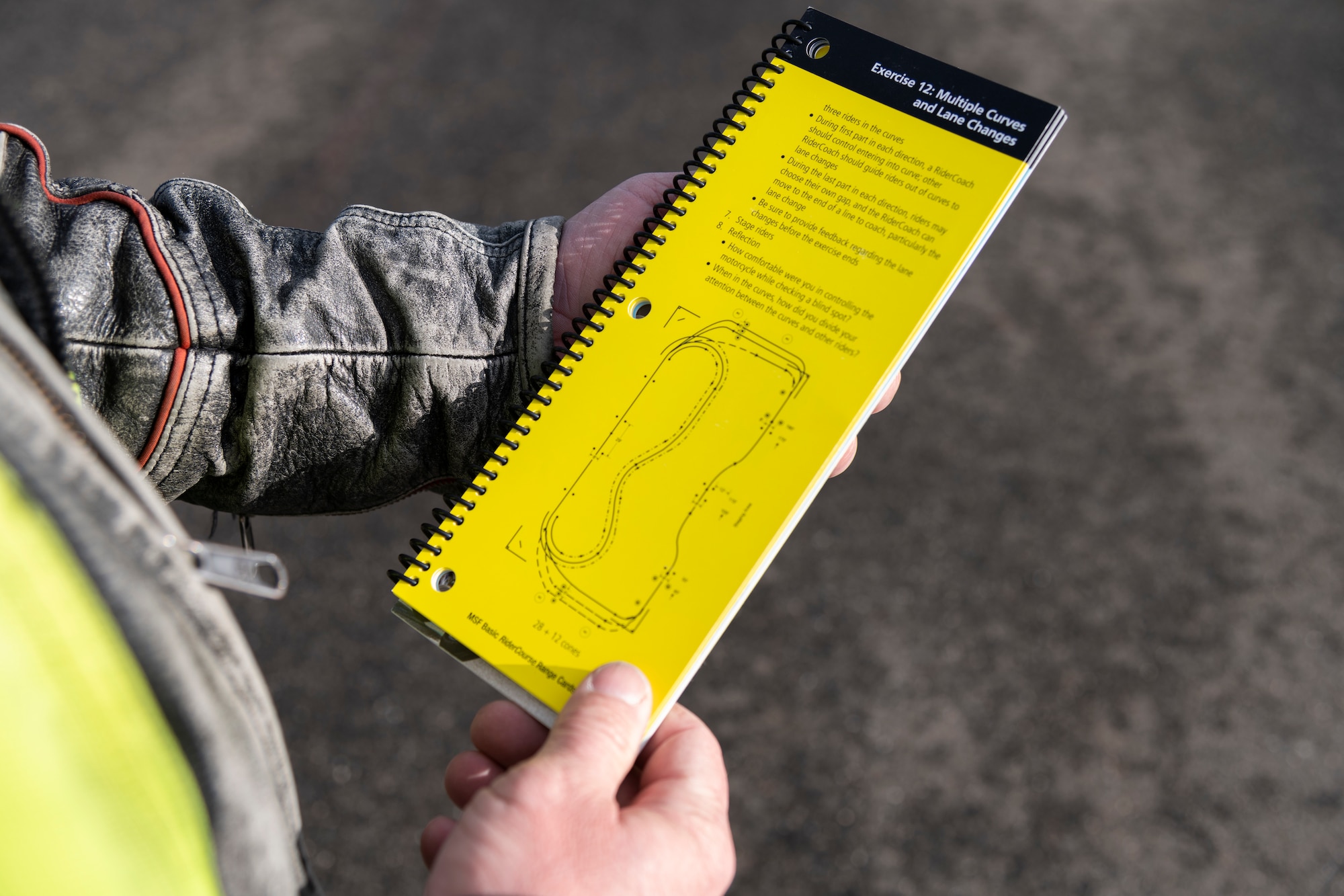 A Rider Coach from the Motorcycle Safety Foundation Rider Coach Trainer Course uses a booklet as a reference for training on Spangdahlem Air Base, Germany, Oct. 22, 2021. Students in the course trained in 14 different exercises over the course of seven days in order to become certified Rider Coach Trainers with MSF. (U.S. Air Force photo by Senior Airman Ali Stewart)