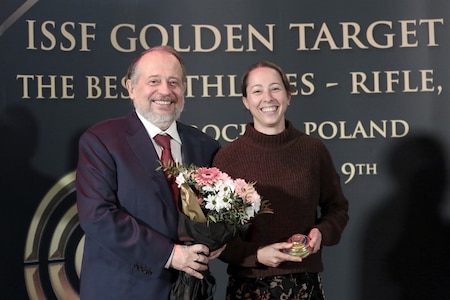 Man and woman posing in front of a backdrop with flowers.