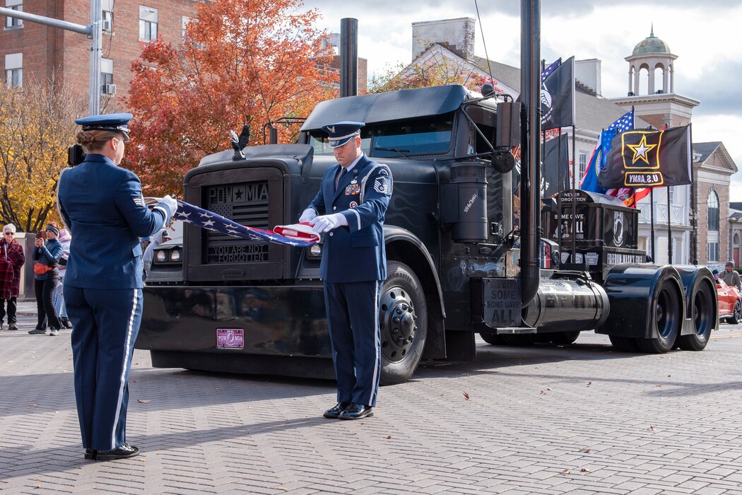 167th Airlift Wing Base Honor Guard members, Senior Airman Caley Arndt and Master Sgt. Justin Byrd, perform a flag folding in front of the Charles Timbrook's “Black Out” Veterans Memorial Truck at the Veteran's Day Parade in Martinsburg, West Virginia, Nov. 13, 2021. The Four State Community Veterans Engagement Board, a veterans advocacy group, organized the parade in Martinsburg to honor area veterans. (U.S. Air National Guard photo by Senior Master Sgt. Emily Beightol-Deyerle)