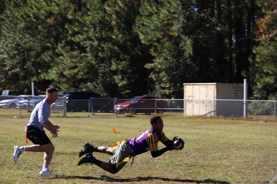 A soldier dives to catch a football while a fellow service member runs behind him.