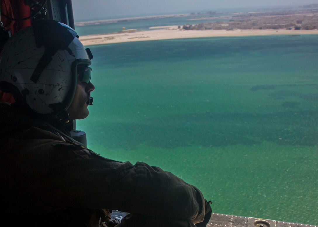 Sailor looks out on the sea from a helicopter.