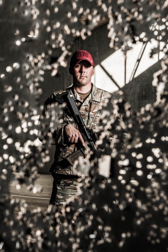 Staff Sgt. Christopher Keller, 436th Security Forces Squadron combat arms instructor, stands behind a marksmanship target riddled with bullet holes Nov. 8, 2021, at Dover Air Force Base, Delaware. Keller is one of five instructors at the Dover AFB Combat Arms Training and Maintenance facility. (U.S. Air Force photo by Mauricio Campino)