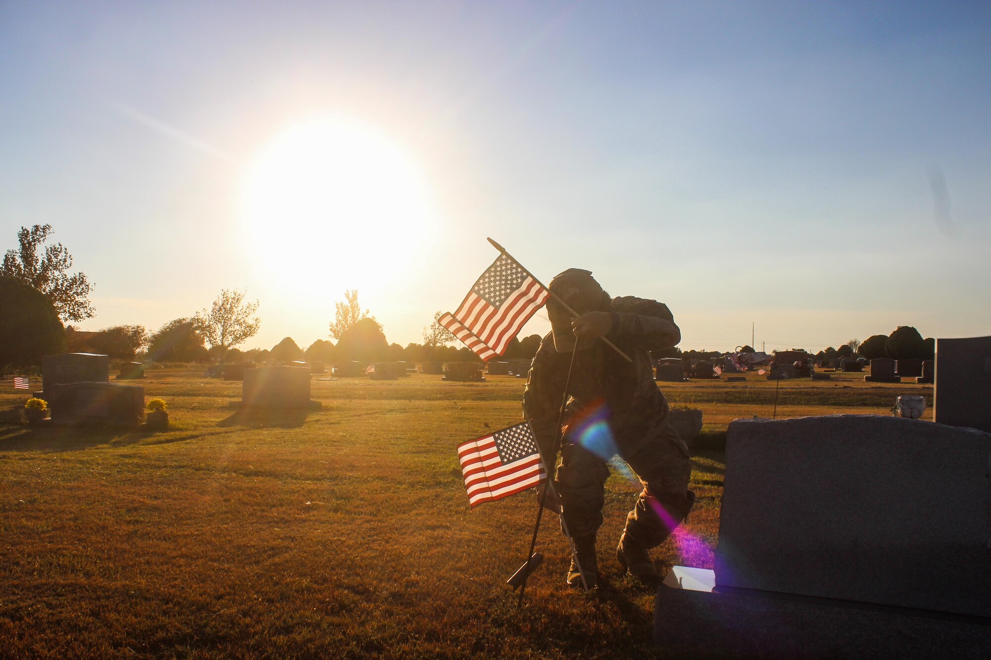 Woman plants flags at cemetery with sunset in background