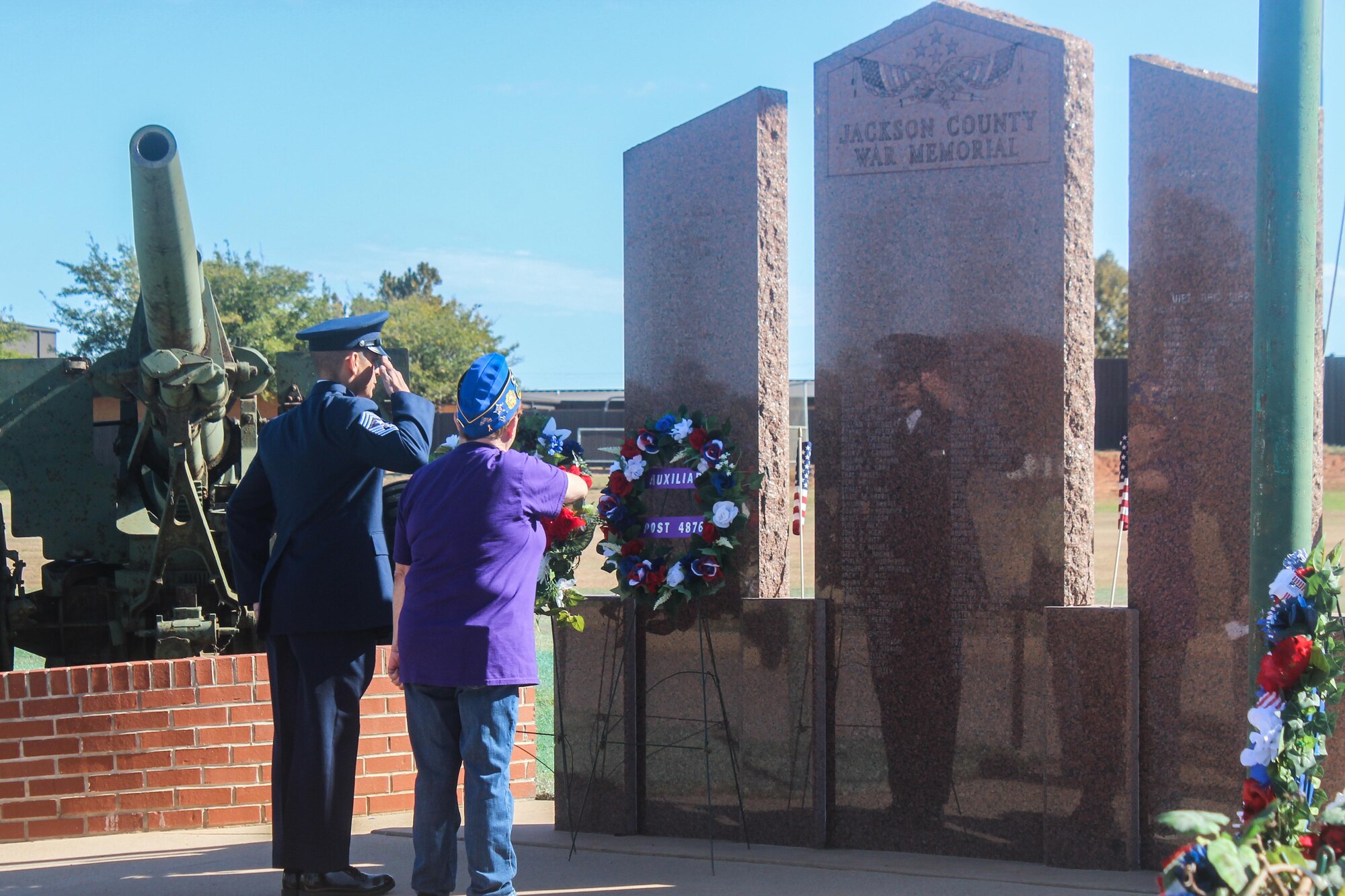 Two individuals salute a war memorial