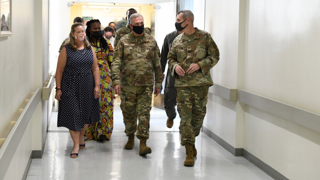 A general and his entourage walk through a hospital corridor.