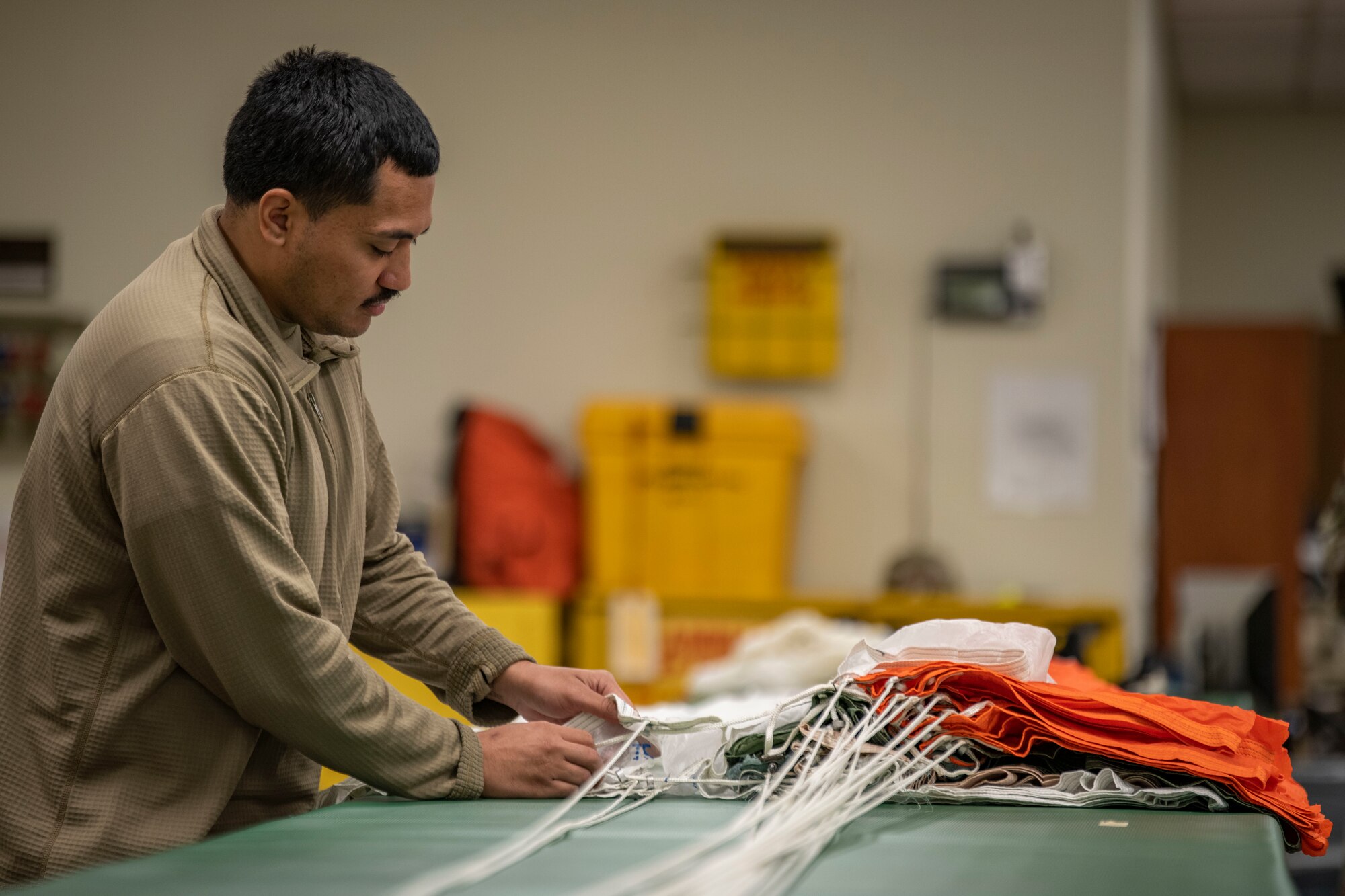 Senior Airman Richard Pena, 8th Operation Support Squadron aircrew flight equipment technician, folds a parachute at Kunsan Air Base, Republic of Korea, Nov. 8, 2021. Aircrew Flight Equipment specialists make sure flyers have the supplies necessary for ensuring that all flight and safety equipment is in the perfect working order.  (U.S. Air Force photo Staff Sgt. Jesenia Landaverde)