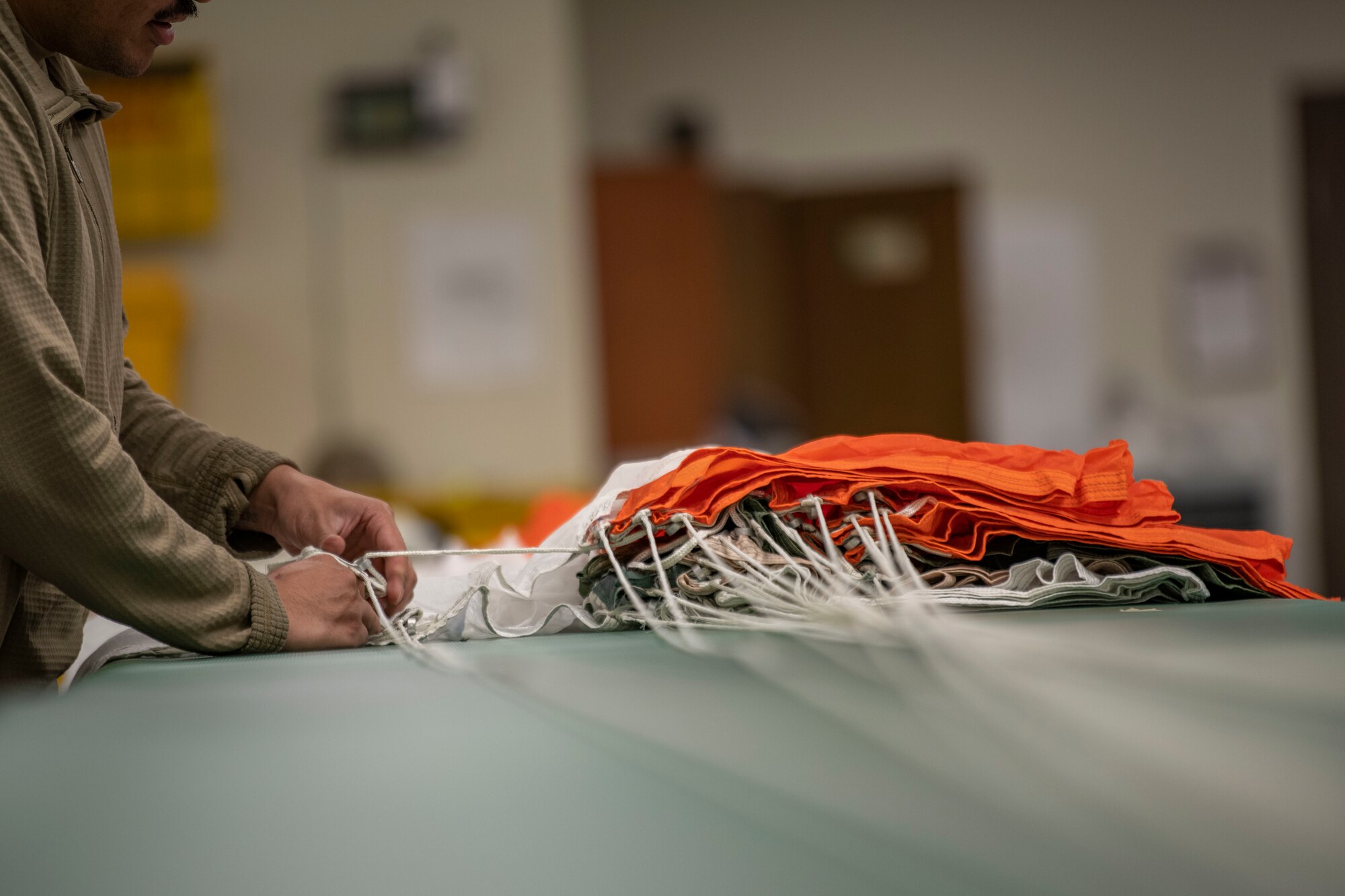 Senior Airman Richard Pena, 8th Operation Support Squadron aircrew flight equipment technician, folds a parachute at Kunsan Air Base, Republic of Korea, Nov. 8, 2021. From packing emergency items like parachutes and survival kits to maintaining regularly used items like oxygen masks, the attention to detail by these Airmen could mean the difference between life and death. (U.S. Air Force photo Staff Sgt. Jesenia Landaverde)