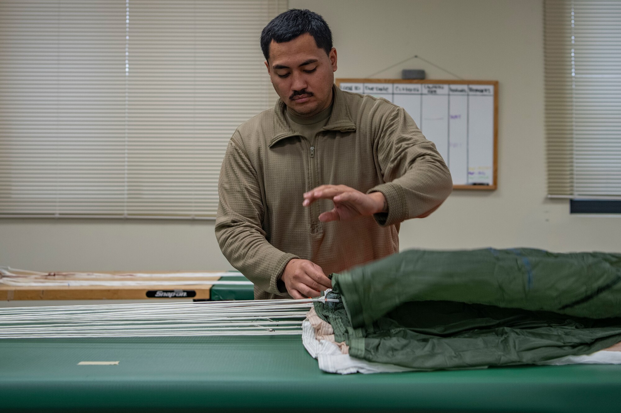 Senior Airman Richard Pena, 8th Operation Support Squadron aircrew flight equipment technician, folds a parachute at Kunsan Air Base, Republic of Korea, Nov. 8, 2021. From packing emergency items like parachutes and survival kits to maintaining regularly used items like oxygen masks, the attention to detail by these Airmen could mean the difference between life and death. (U.S. Air Force photo Staff Sgt. Jesenia Landaverde)