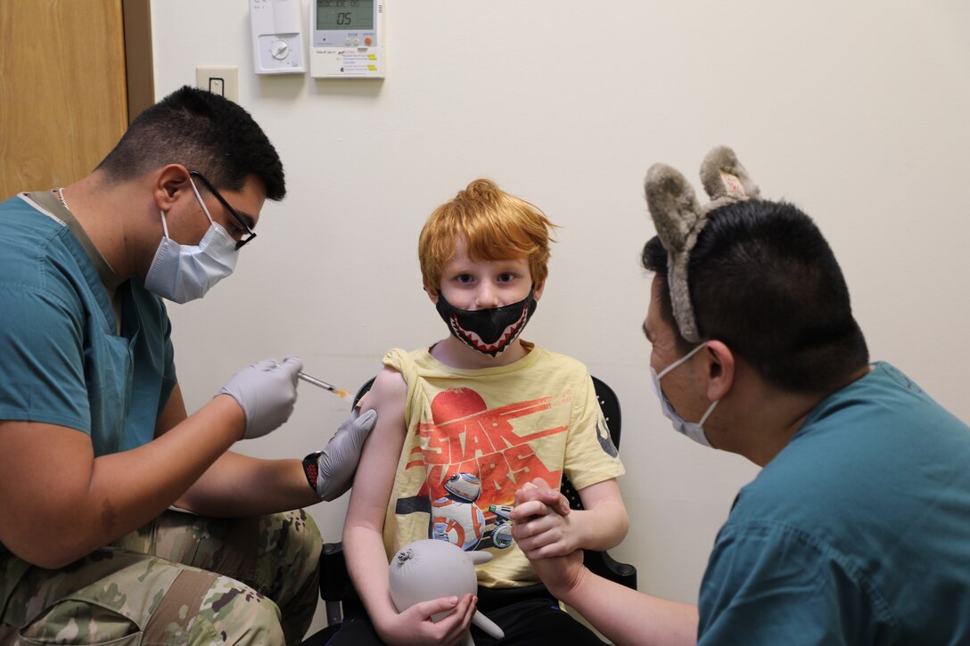 CAMP HUMPHREYS, South Korea – Will Henjum (middle), a 7 year old boy, receives the first dose of Pfizer-BioNTech pediatric COVID-19 vaccine on Nov. 17, 2021 at the Camp Humphreys COVID-19 Vaccination Center. BDAACH’s COVID-19 Vaccination Center started offering the vaccine to age 5 to 11 children within U.S. Forces Korea this day. (U.S. Army Photo by Inkyeong Yun, Brian D. Allgood Army Community Hospital public affairs)