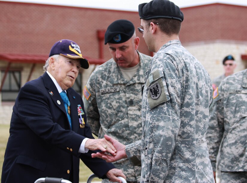 An older man hands a coin to a uniformed soldier while others stand by.