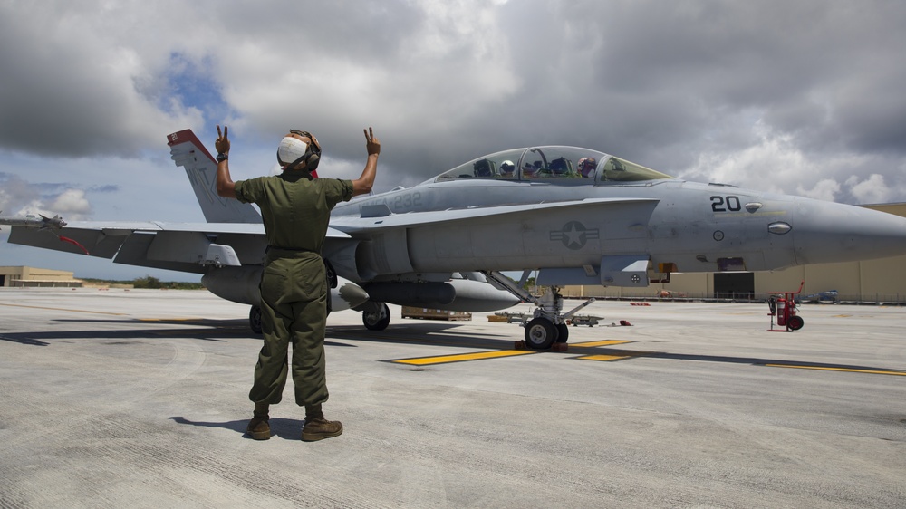 A Marine signaling with both hands to a Hornet pilot.