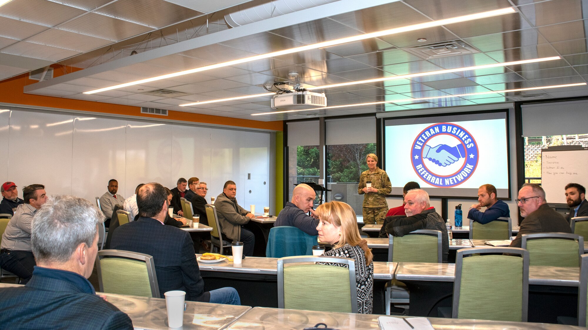 A woman in Air Force uniform briefs a group in a conference room.