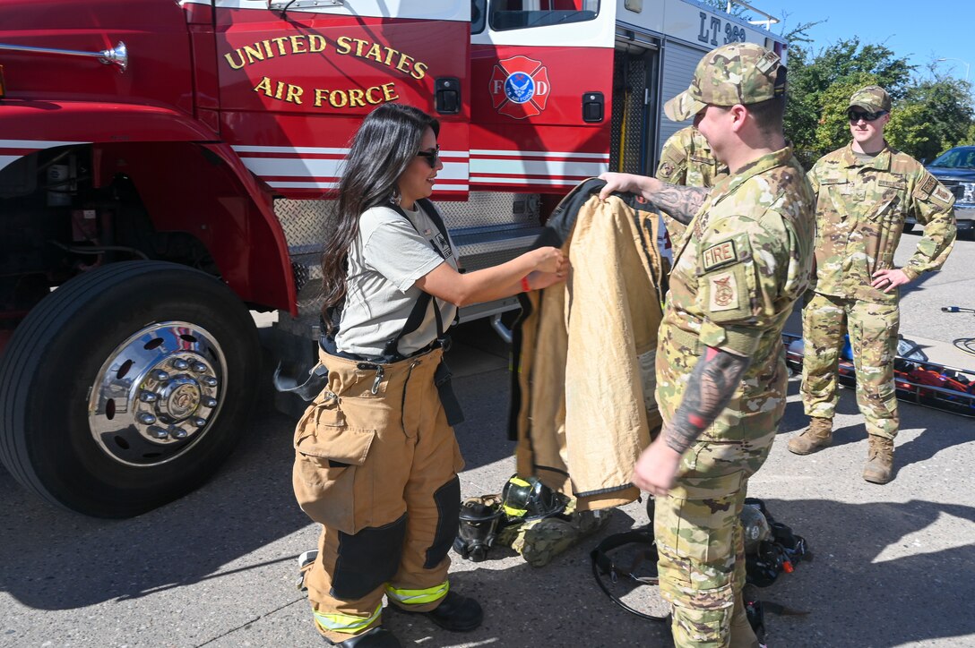 Elizabeth Canchola, football game attendee, tries on firefighting equipment at a Salute to Service event with the help of U.S. Air Force Senior Airman Craig Dennis, 944th Civil Engineer Squadron driver/operator, Nov. 14, 2021, at the State Farm Stadium, Glendale, Arizona.