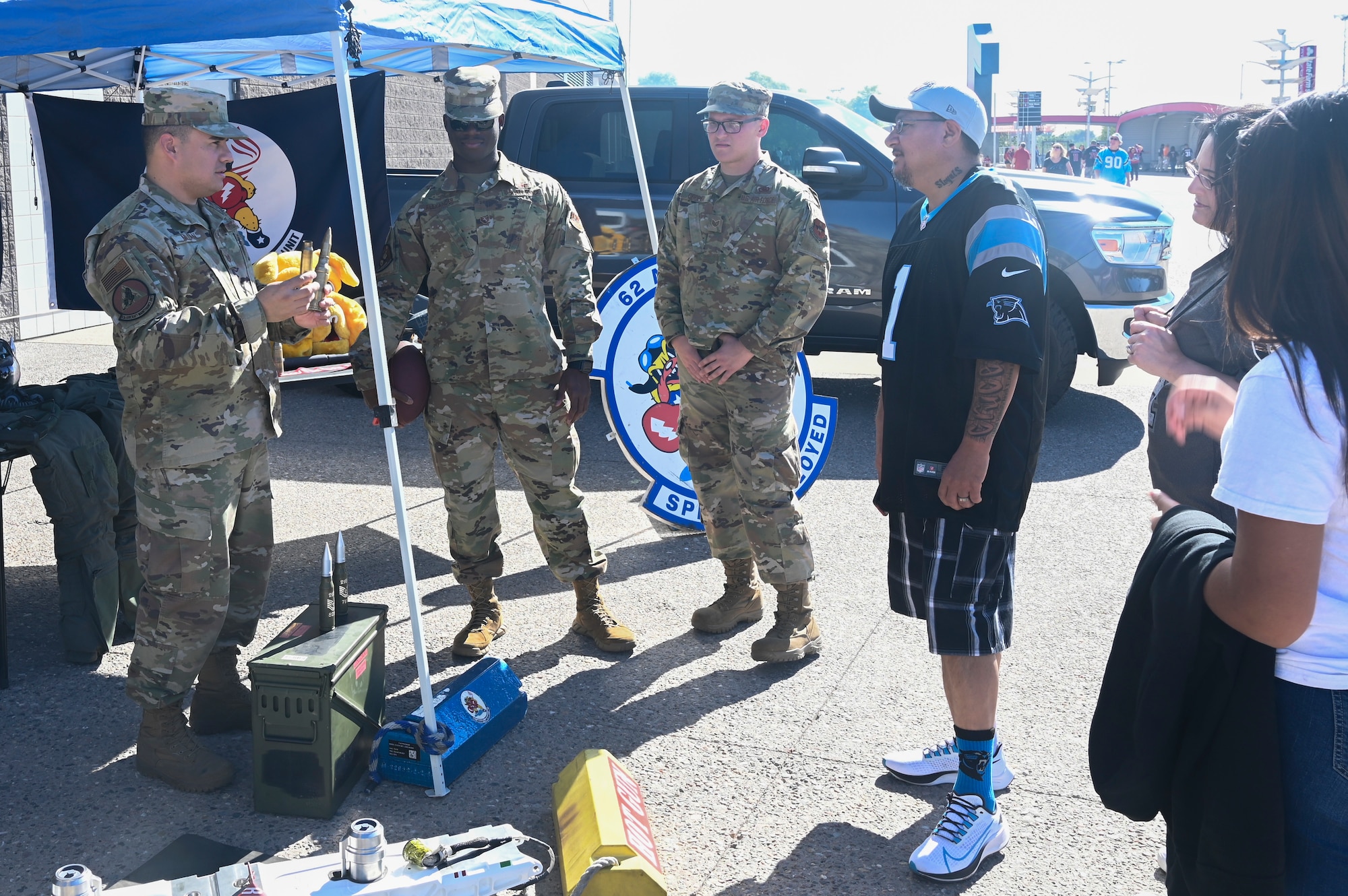 U.S. Air Force Tech. Sgt. Hector Millan, 63rd Aircraft Maintenance Unit weapons expeditor, shows different ammo rounds to football fans alongside U.S. Air Force Staff Sgt. Donte Alexander, 63rd AMU dedicated crew chief, and U.S. Air Force Staff Sgt. Jacob Cooper, 62nd AMU integrated assistant dedicated crew chief, Nov. 14, 2021, at the State Farm Stadium, Glendale, Arizona.
