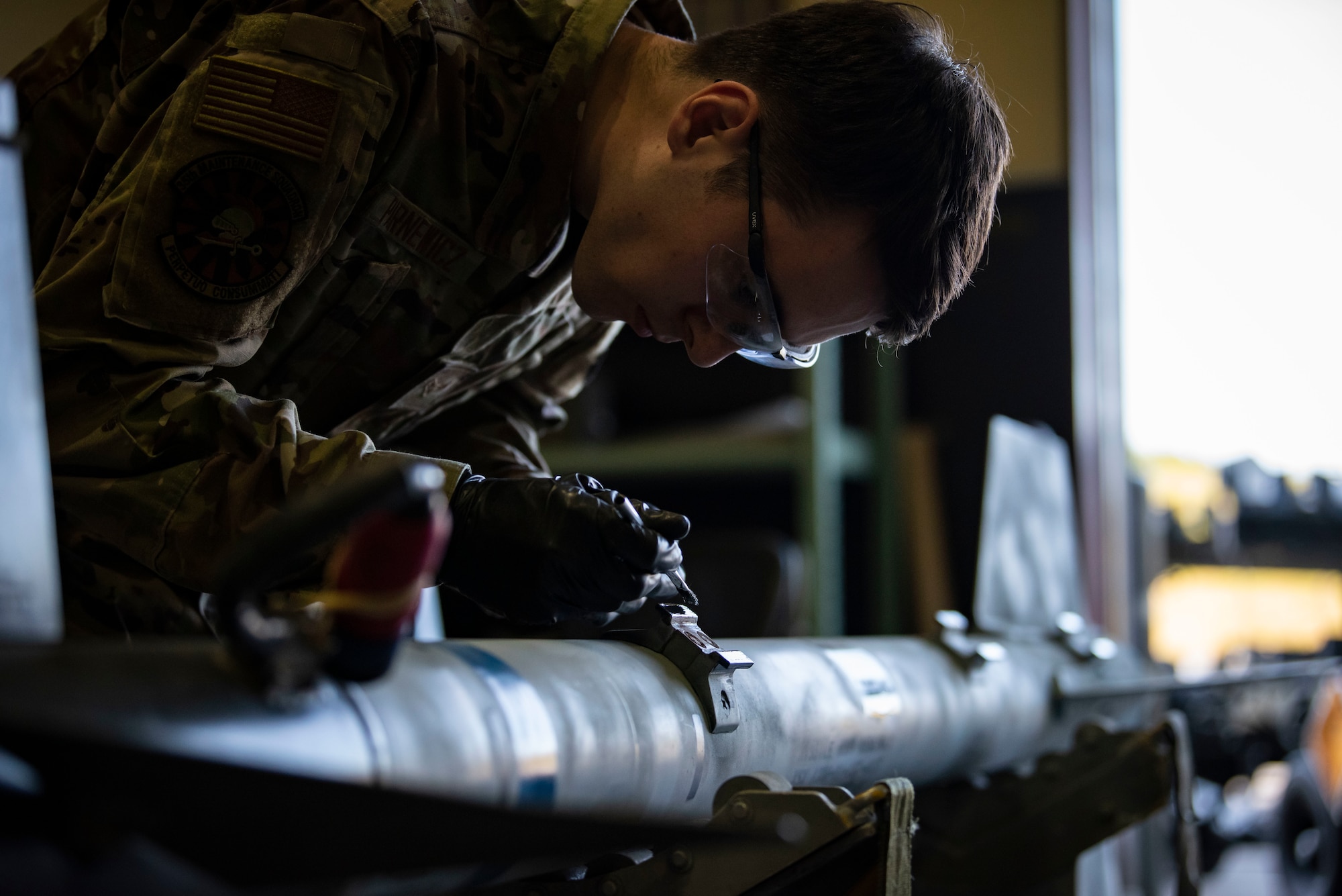 Service member in uniform paints the side of a missile.