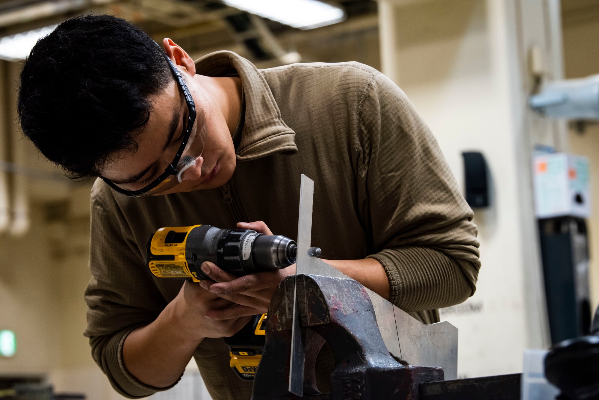 Service member operates a a drill to cut metal.