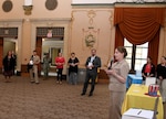 Female holding microphone addressing crowd at an indoor event.