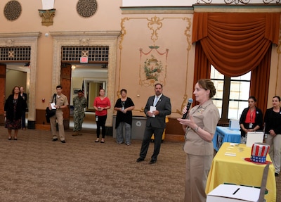 Female holding microphone addressing crowd at an indoor event.