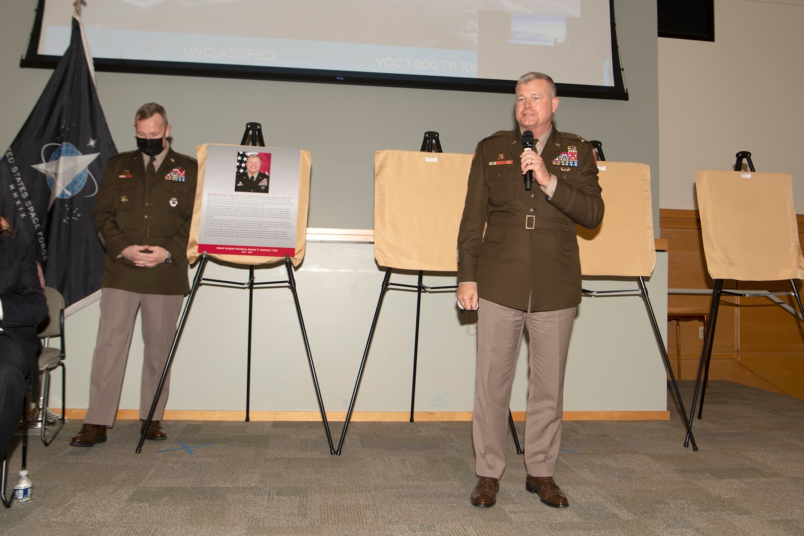 two Army generals speak on stage in dress uniforms