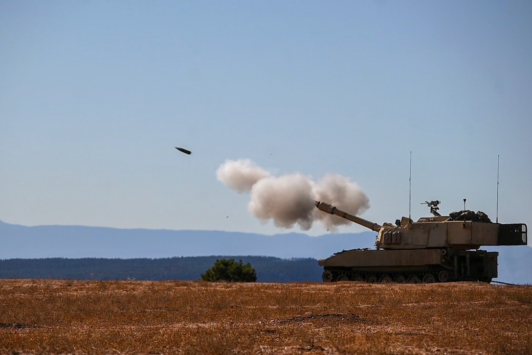 Soldiers fire an armored vehicle in a field.