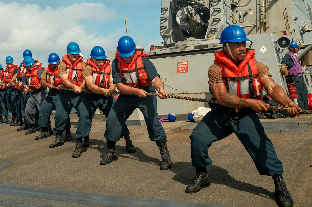 Sailors standing in a line pull a rope.