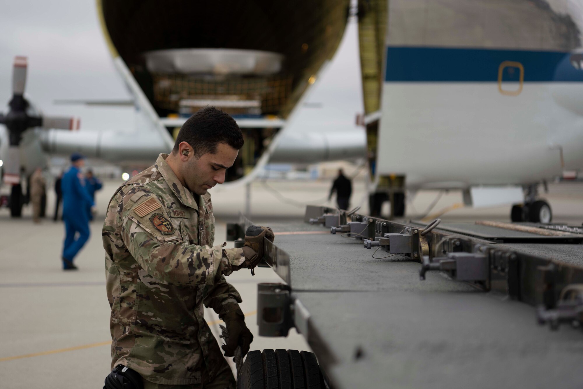 An Airman places an object behind a tire of a vehicle