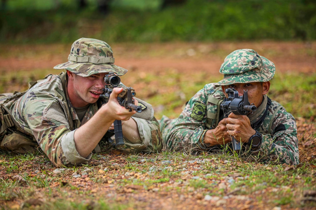 Two service members lie on the ground pointing their weapons.