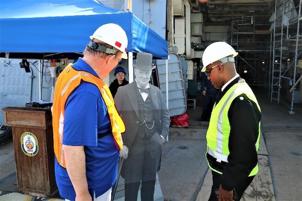 The Hon. Rupert Soames, OBE, and Cmdr. Brian Anthony, commanding officer, USS Winston S. Churchill, behold the cardboard cutout of Sir Winston Churchill, the ship’s namesake, who has graced many command photos on USS Winston S. Churchill’s Facebook page.