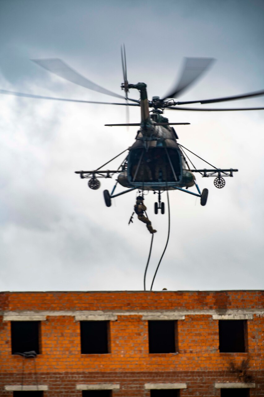 Soldier rappels from a helicopter to a building.