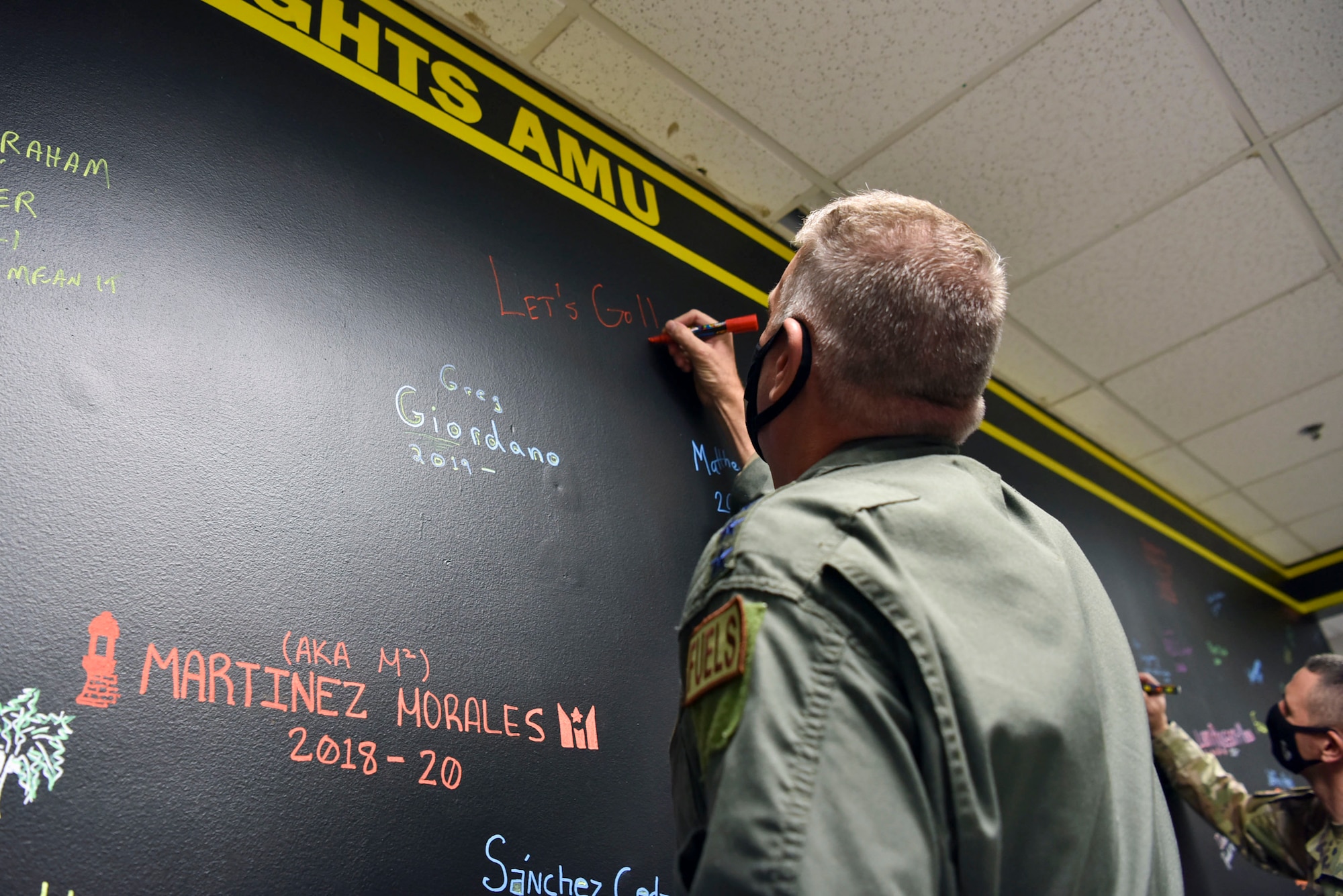 Gen. Minihan signs his name and his mantra 'Let's Go!' on a wall.