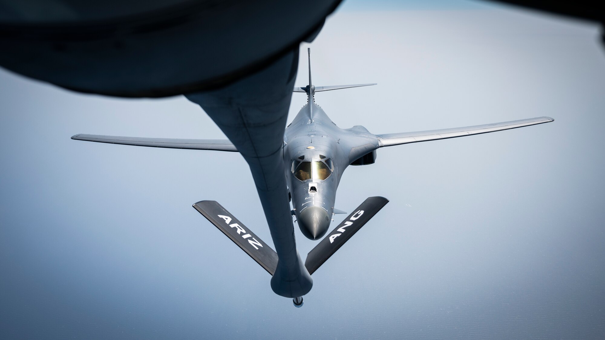 Photo looking at a U.S. Air Force B-1B Lancer flying over the ocean from a KC-135 Stratotanker boom operator window.