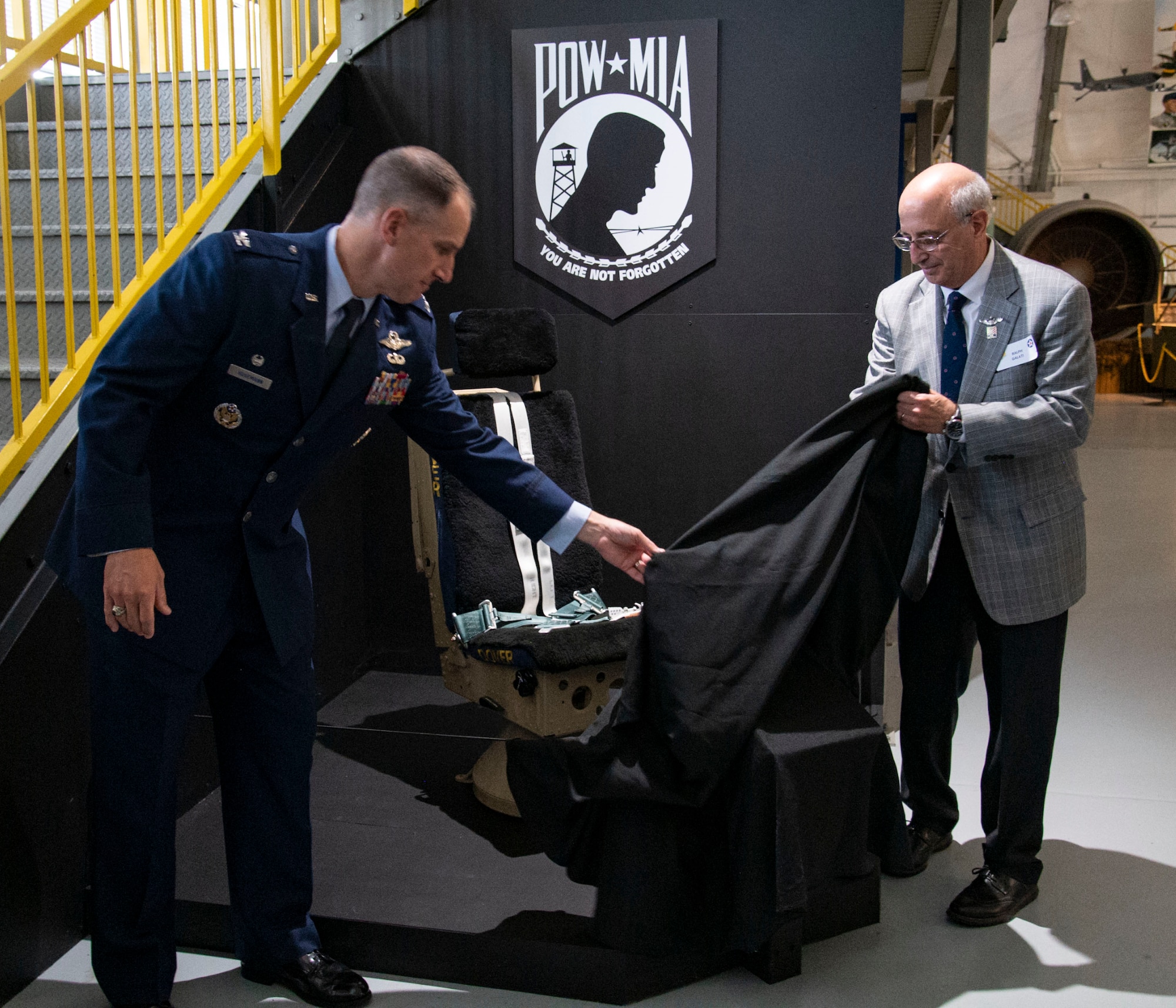 Col. Matt Husemann, left, 436th Airlift Wing commander, and former prisoner of war Ralph Galati, unveil the Chair of Honor during a ceremony at the Air Mobility Command Museum on Dover Air Force Base, Delaware, Nov. 11, 2021. The chair is one of 58 dedicated chairs of honor throughout the state of Delaware and the first aircraft chair. (U.S. Air Force photo by Roland Balik)