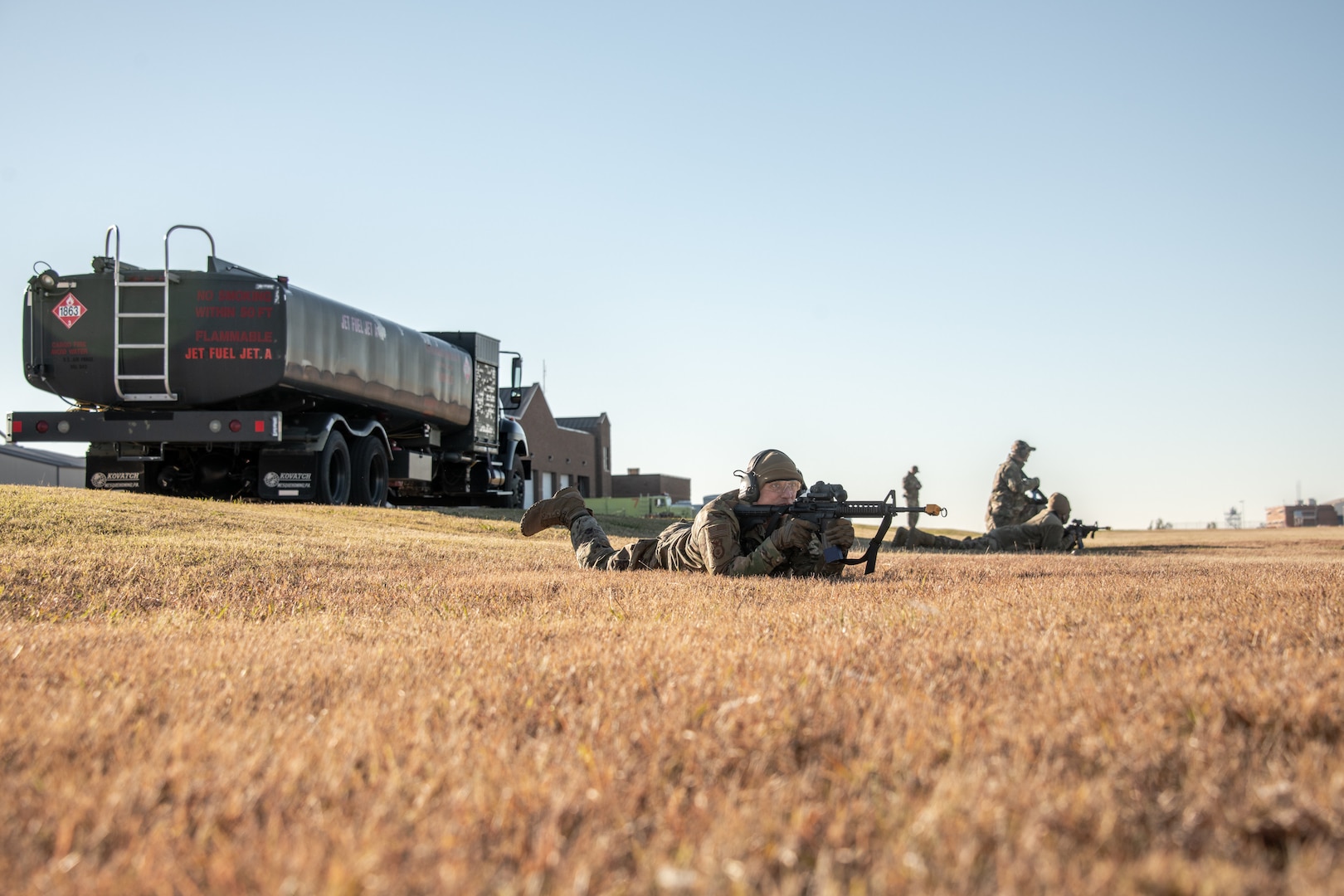 man lies prone holding rifle in front of fuel truck