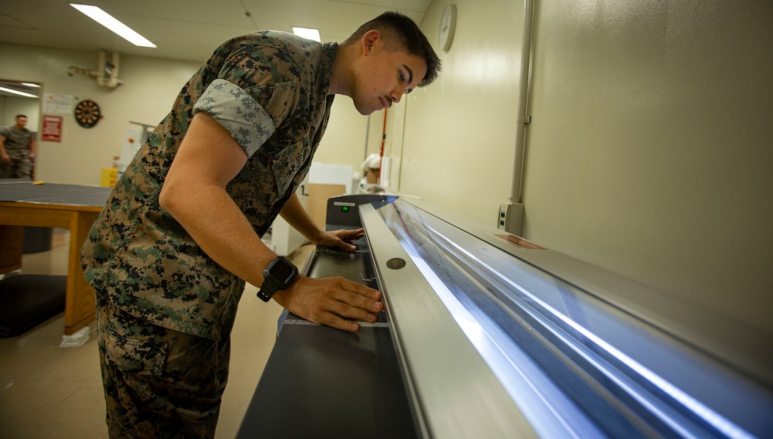 U.S. Marine Corps Lance Cpl. Hunter Barber, a combat graphics specialist with Communication Strategy and Operations, Combat Logistics Regiment 37, 3rd Marine Logistics Group, cuts out a poster on Camp Foster, Okinawa, Japan, Nov. 5, 2021. Barber is a White Mountain Apache tribal member who grew up on the Fort Apache reservation in Arizona. "Resilient and Enduring: We Are Native People" is the November 2021 theme to honor the past and present Native American Marines who continue to pave the way for future generations. (U.S. Marine Corps photo by Cpl. Karis Mattingly)