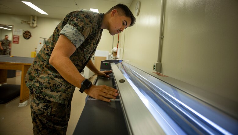U.S. Marine Corps Lance Cpl. Hunter Barber, a combat graphics specialist with Communication Strategy and Operations, Combat Logistics Regiment 37, 3rd Marine Logistics Group, cuts out a poster on Camp Foster, Okinawa, Japan, Nov. 5, 2021. Barber is a White Mountain Apache tribal member who grew up on the Fort Apache reservation in Arizona. "Resilient and Enduring: We Are Native People" is the November 2021 theme to honor the past and present Native American Marines who continue to pave the way for future generations. (U.S. Marine Corps photo by Cpl. Karis Mattingly)
