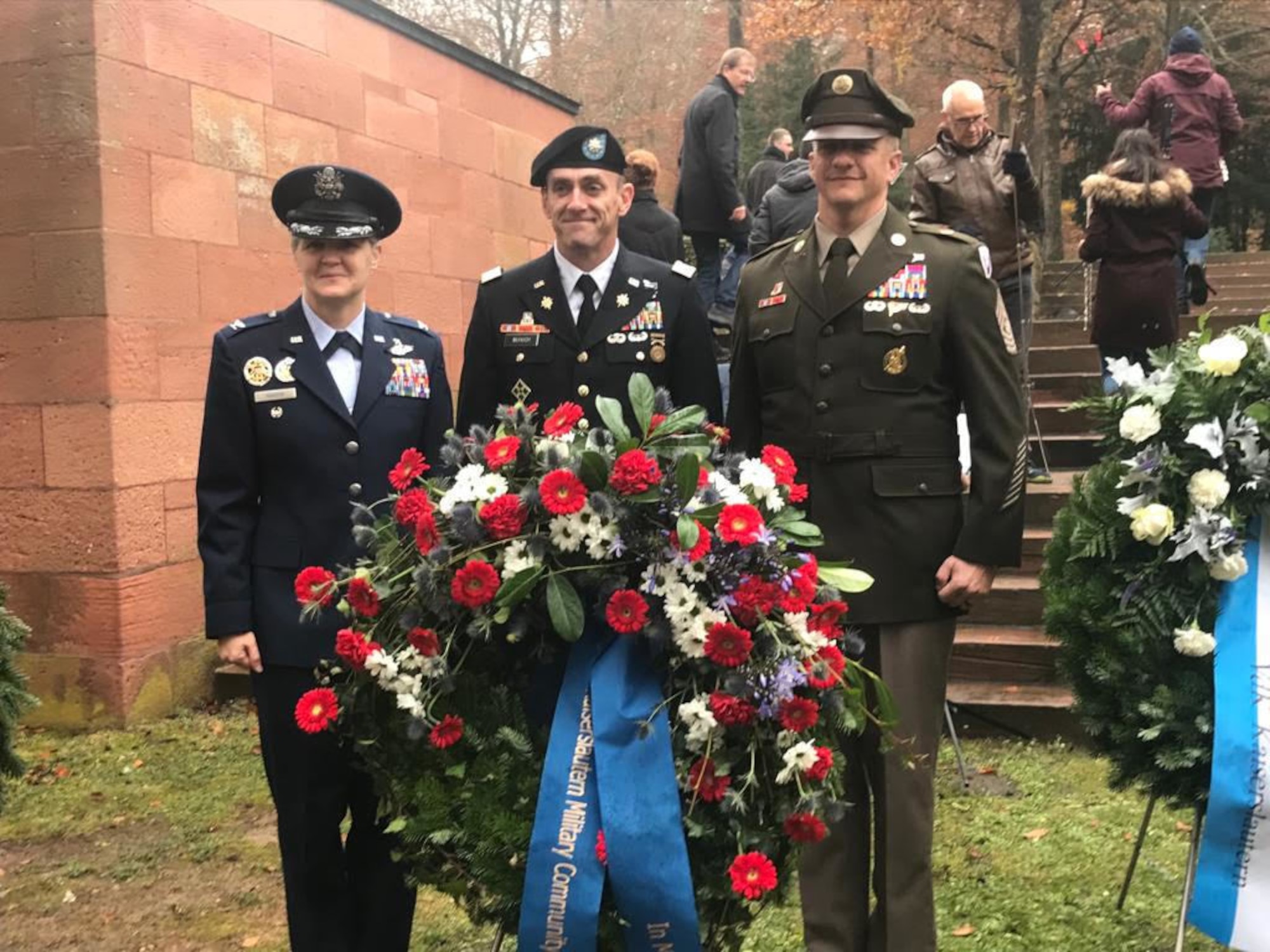 Three military members standing behind a floral wreath.